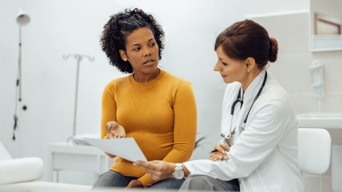 Black woman and white medical professional looking at a piece of paper in an office.